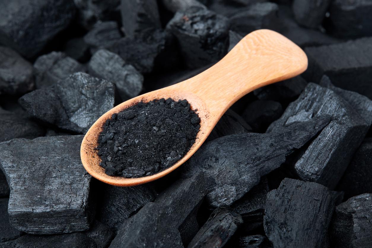 Powdered charcoal is contained in a wooden spoon atop a pile of bricks of charcoal.