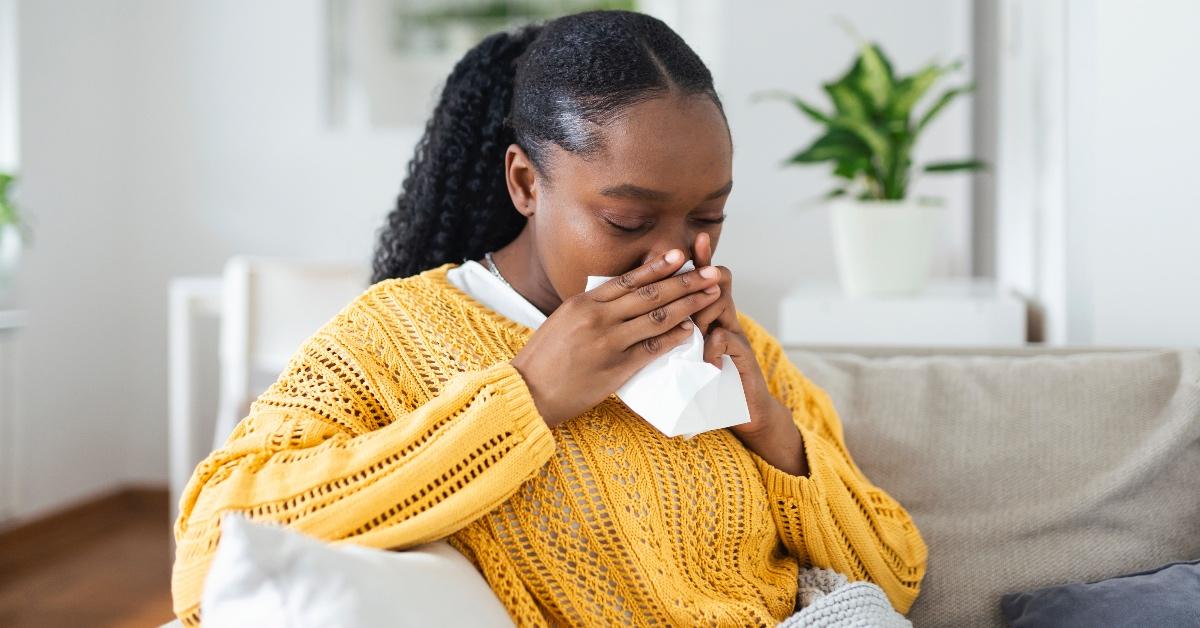 A woman in a yellow sweater blowing her nose.