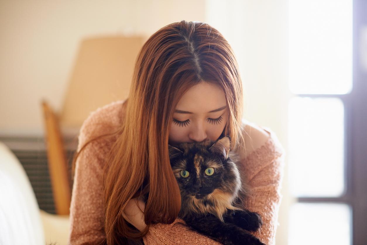 A young woman holds a cat in her arms while bringing her lips and nose to the cat's head.