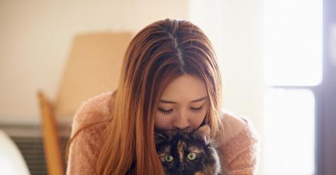 A young woman holds a cat in her arms while bringing her lips and nose to the cat's head.