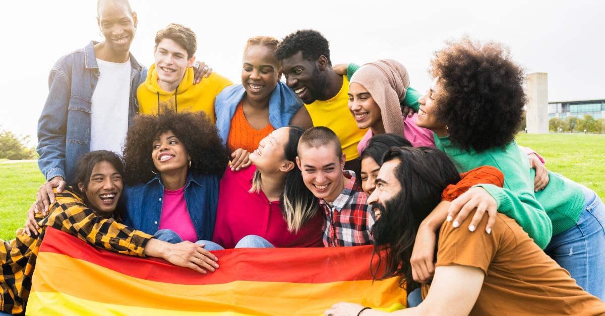 Group of people smiling and holding a rainbow LGBTQ+ flag at an outdoor Pride event