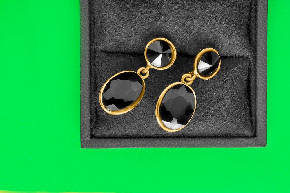 A pair of black onyx earrings in a box against a green background.