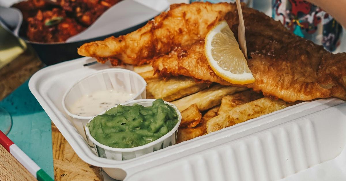 Plastic takeout container with fried fish and french fries, as well as two dipping sauces.