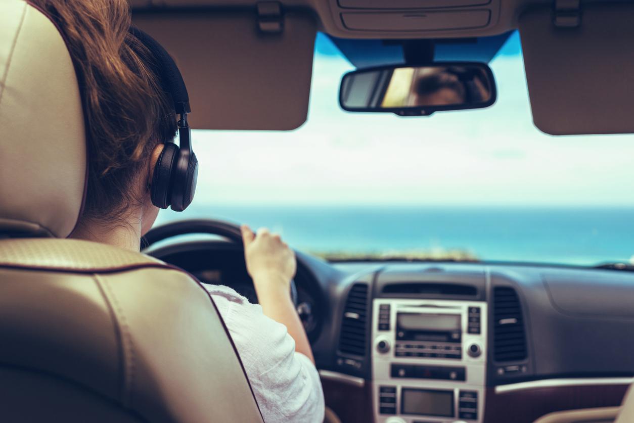 A woman wearing black headphones is photographed from behind while driving a car.