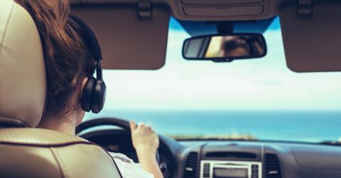 A woman wearing black headphones is photographed from behind while driving a car.