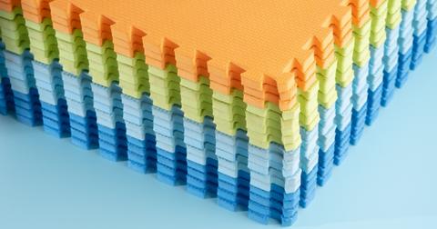 Close up of a stack of thin, orange, green, light blue, and dark blue foam mats.