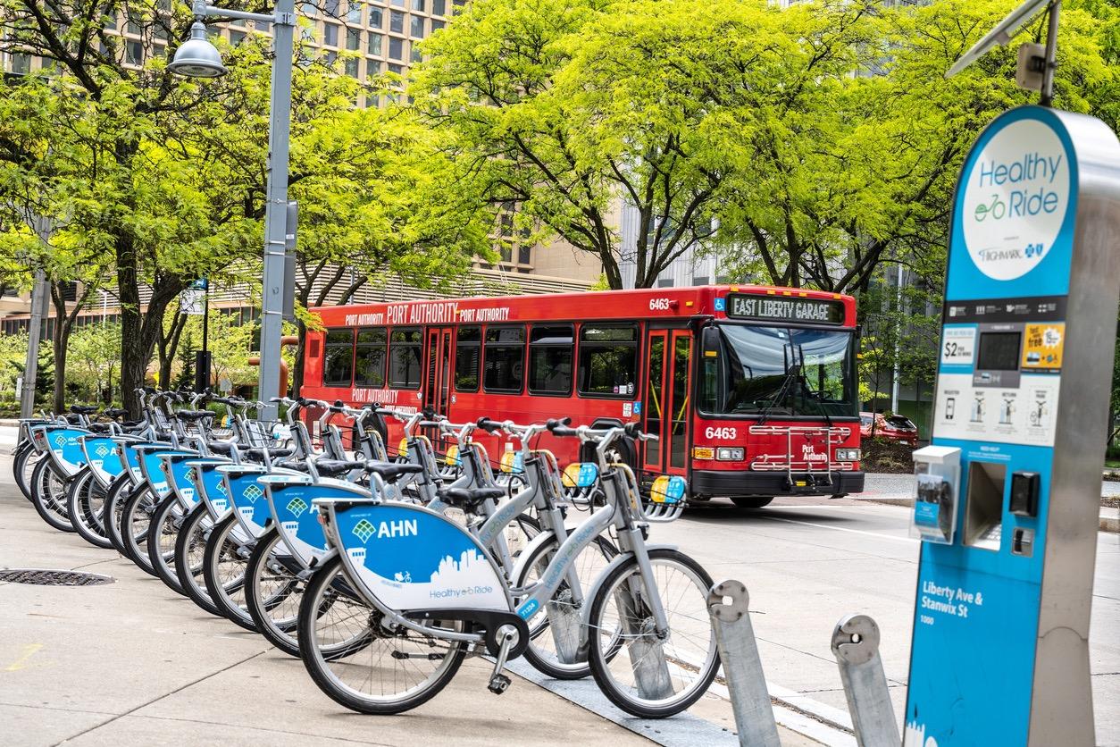 A red bus drives past a rack of rental bicycles on a city street