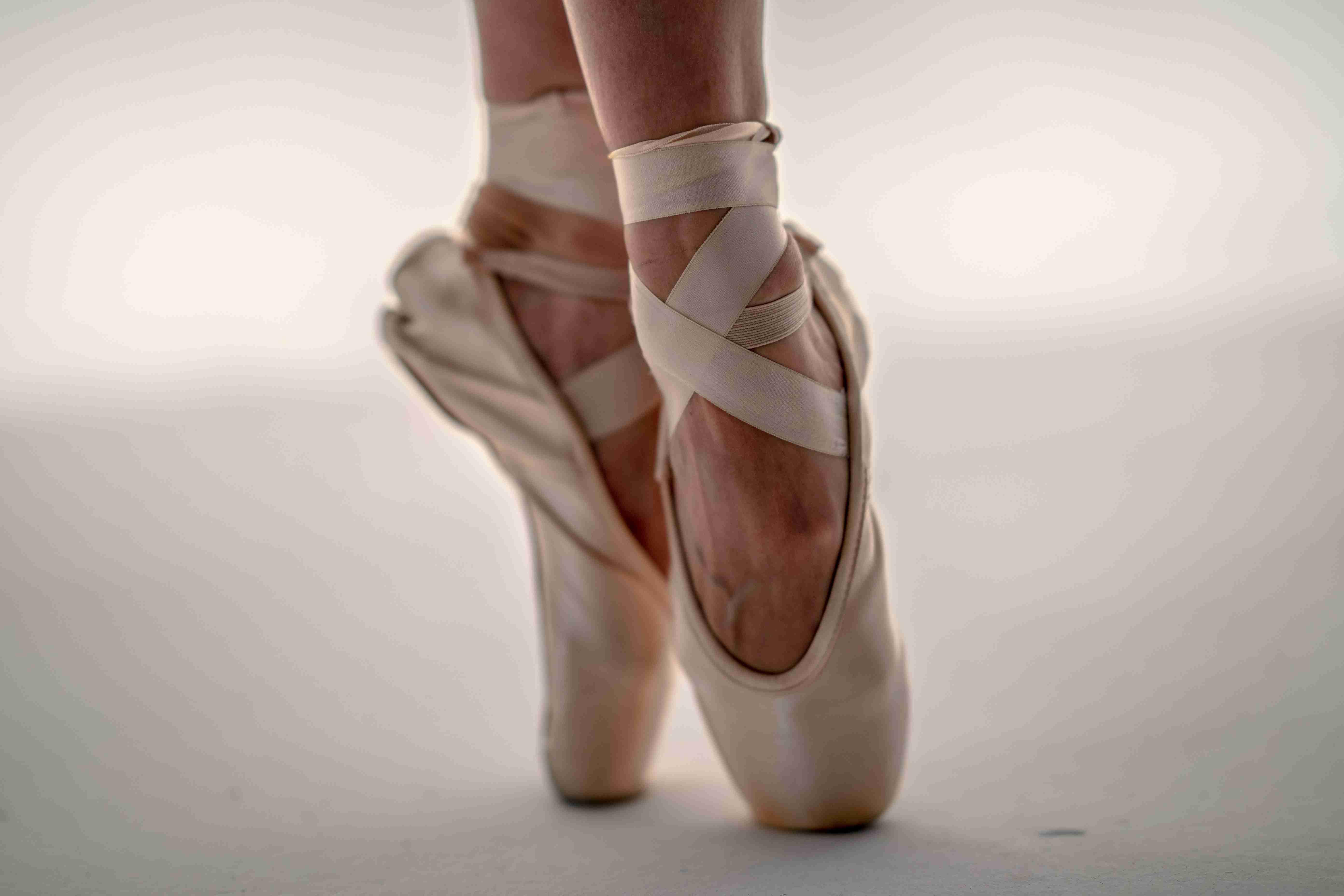 A ballerina's ballet shoes are pictured from the ankle down atop a gray floor.