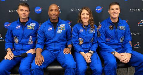Astronauts sit together in blue suits while answering questions about space mission