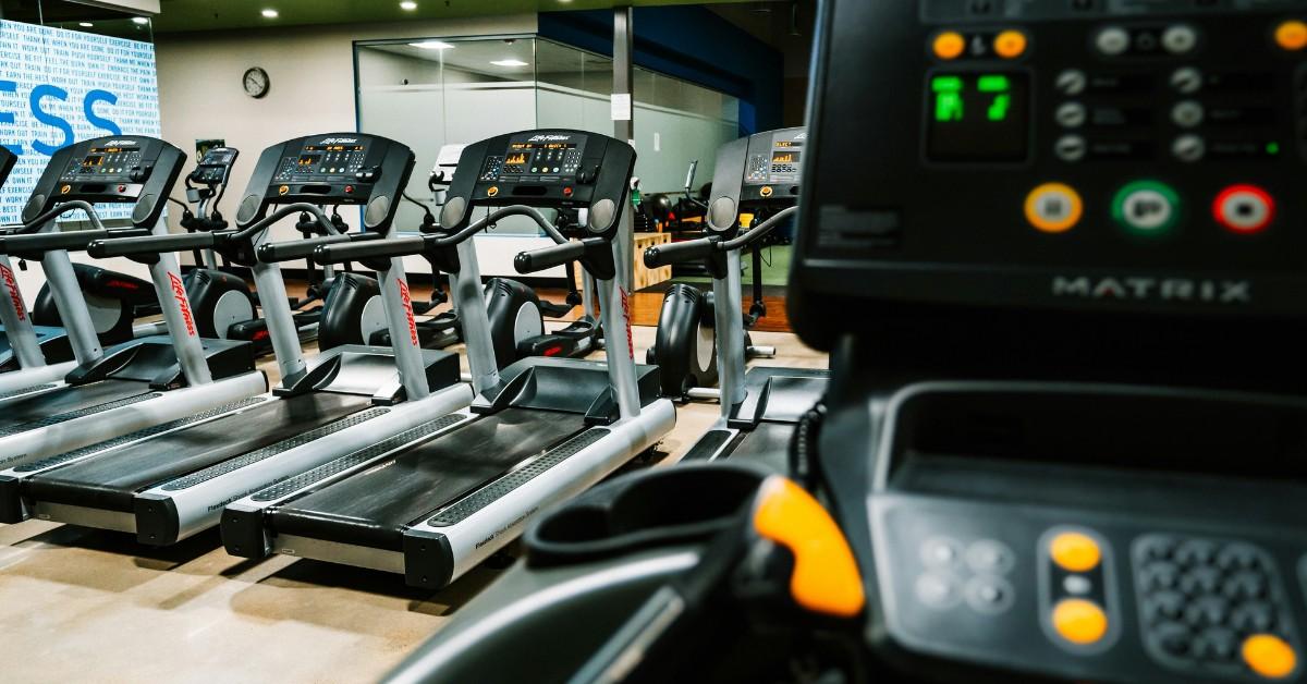 A row of empty treadmills sit next to each other at a gym