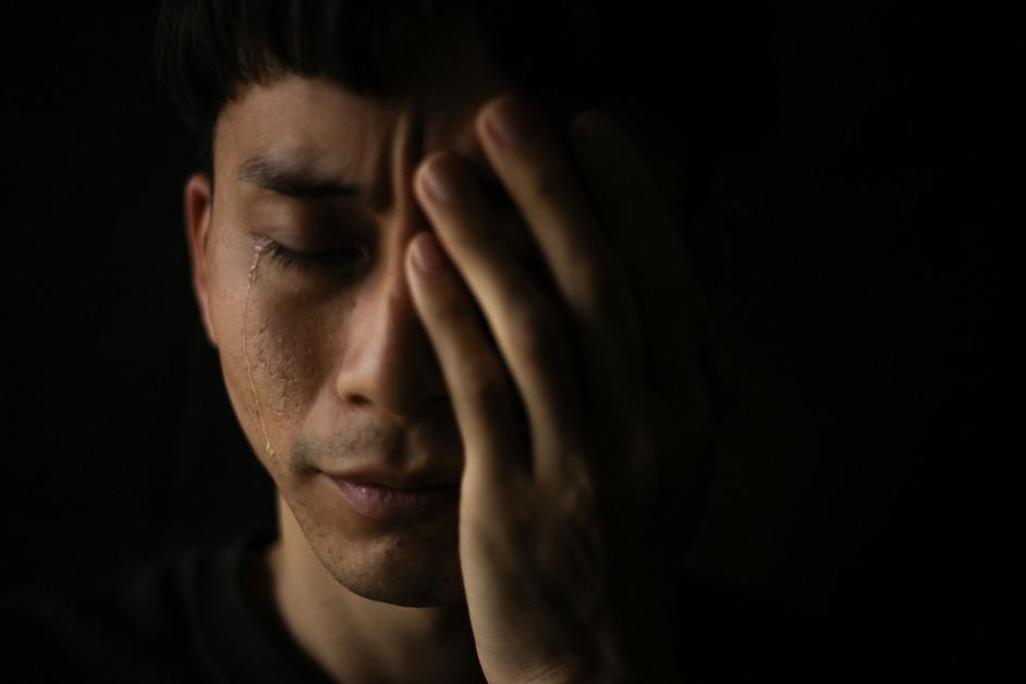 A man holds a hand to his face while crying in front of a dark background. 