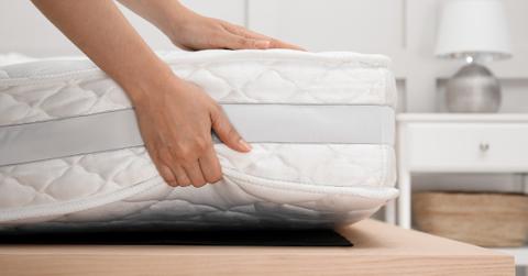 hands placing a mattress on a wooden bed frame in a bedroom