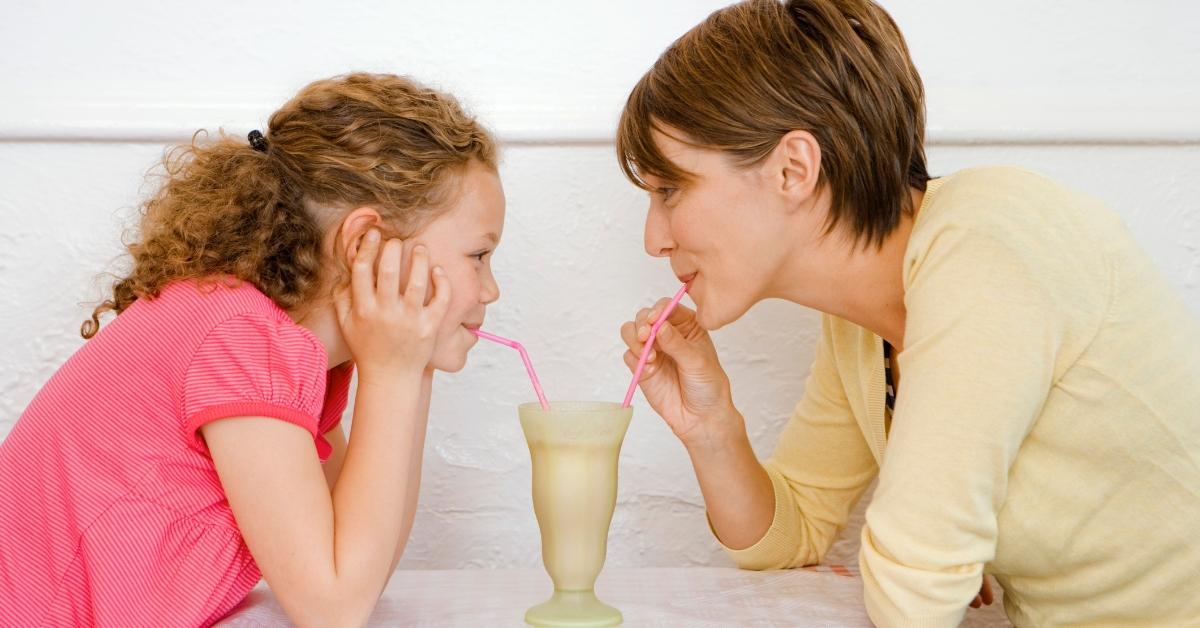 A girl and her mother sharing a milkshake. 