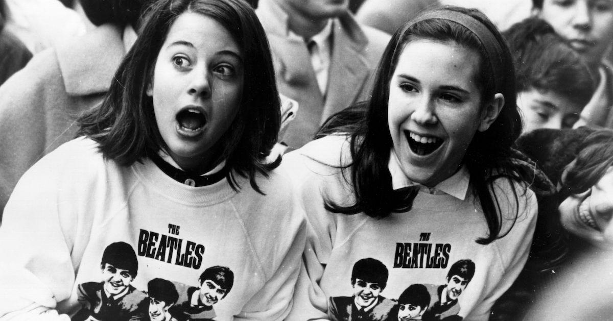 Black and white shot of two excited girls in Beatles sweatshirts, amongst a crowd of fans in New York, welcoming the group as they arrive at the airport, on Feb. 10, 1964.