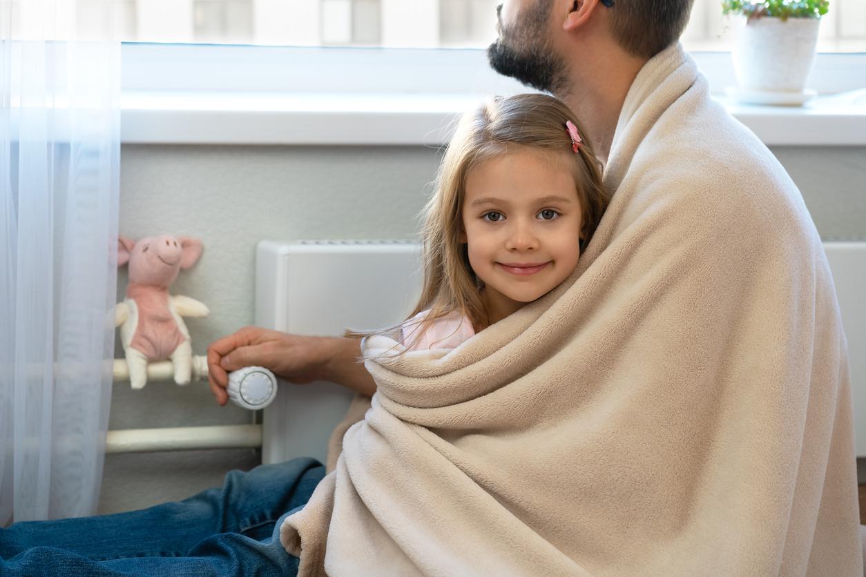 A smiling child is wrapped in a beige blanket while sitting on her father's lap.