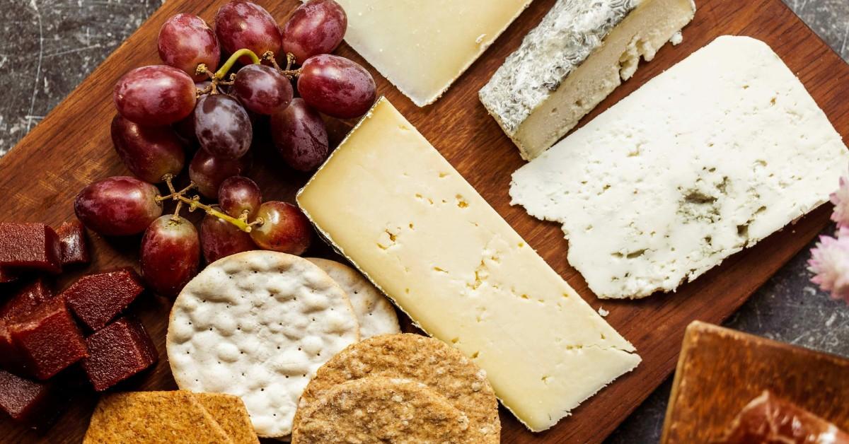 Cheese, crackers, bread, and fruit sit on a snack board