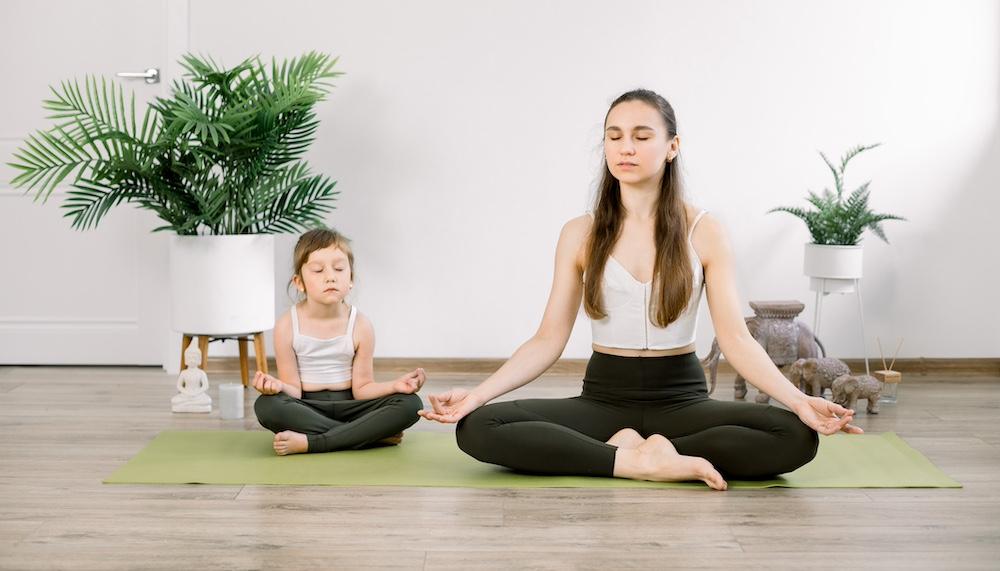 A mother and daughter doing yoga together indoors. 