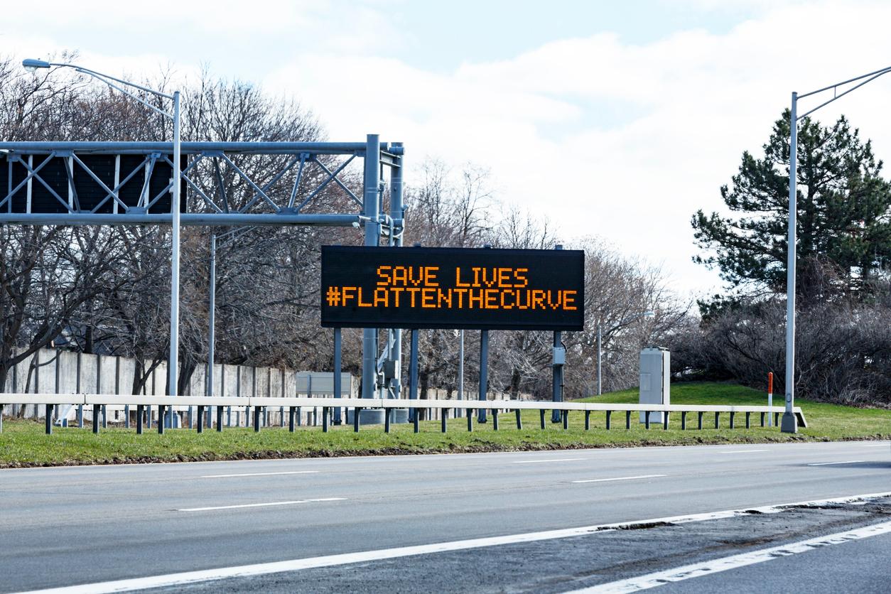 Beside a highway is a digital sign that reads "save lives #flattenthecurve"