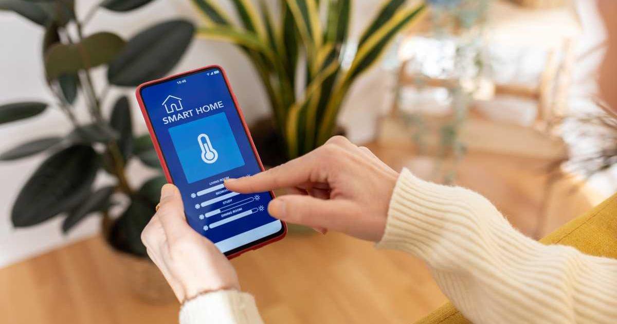 A young woman holding a smartphone using IOT smart home app to change the household temperature. (Representative Cover Image Source: Getty Images | Xavier Lorenzo)