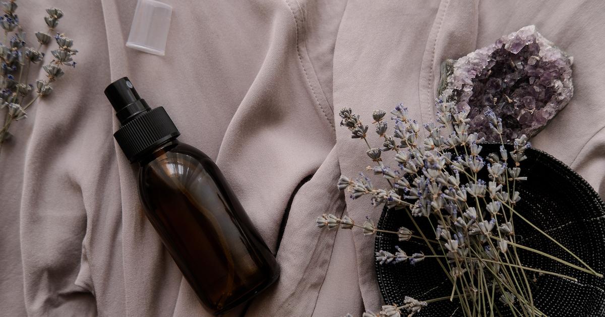 Amber spray bottle on a bed next to a bundle of lavender and a purple crysatal