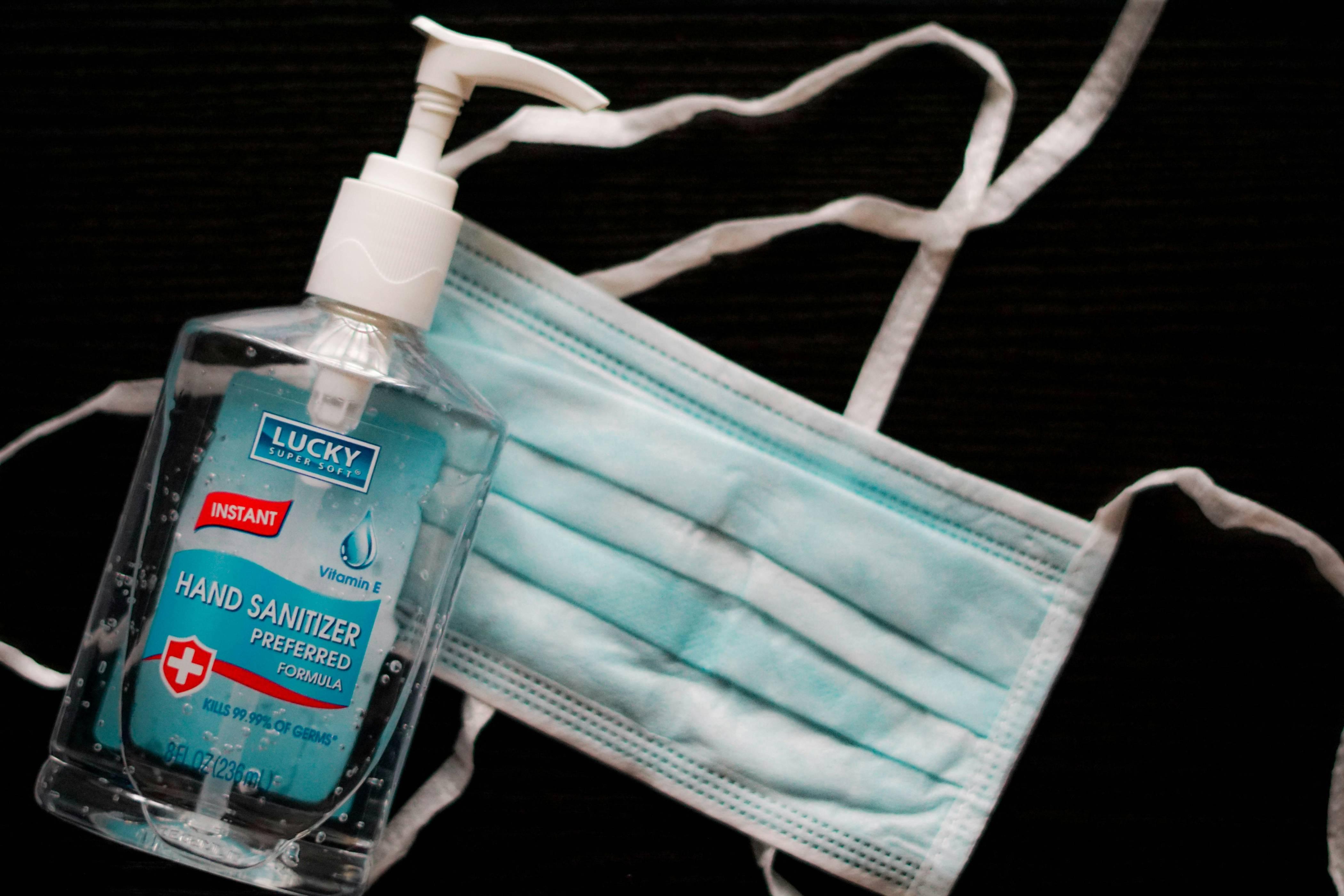A blue face mask and bottle of hand sanitizer are pictured atop a black table.