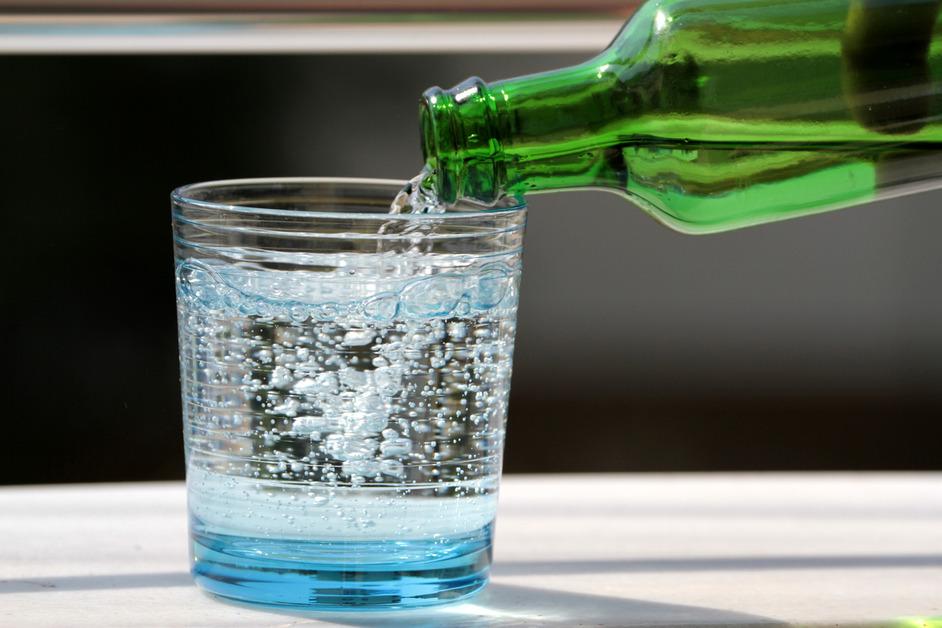 A green glass bottle pours sparkling water into a small glass. 