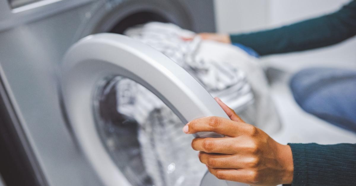 Person places bundle of white clothing into a washing machine