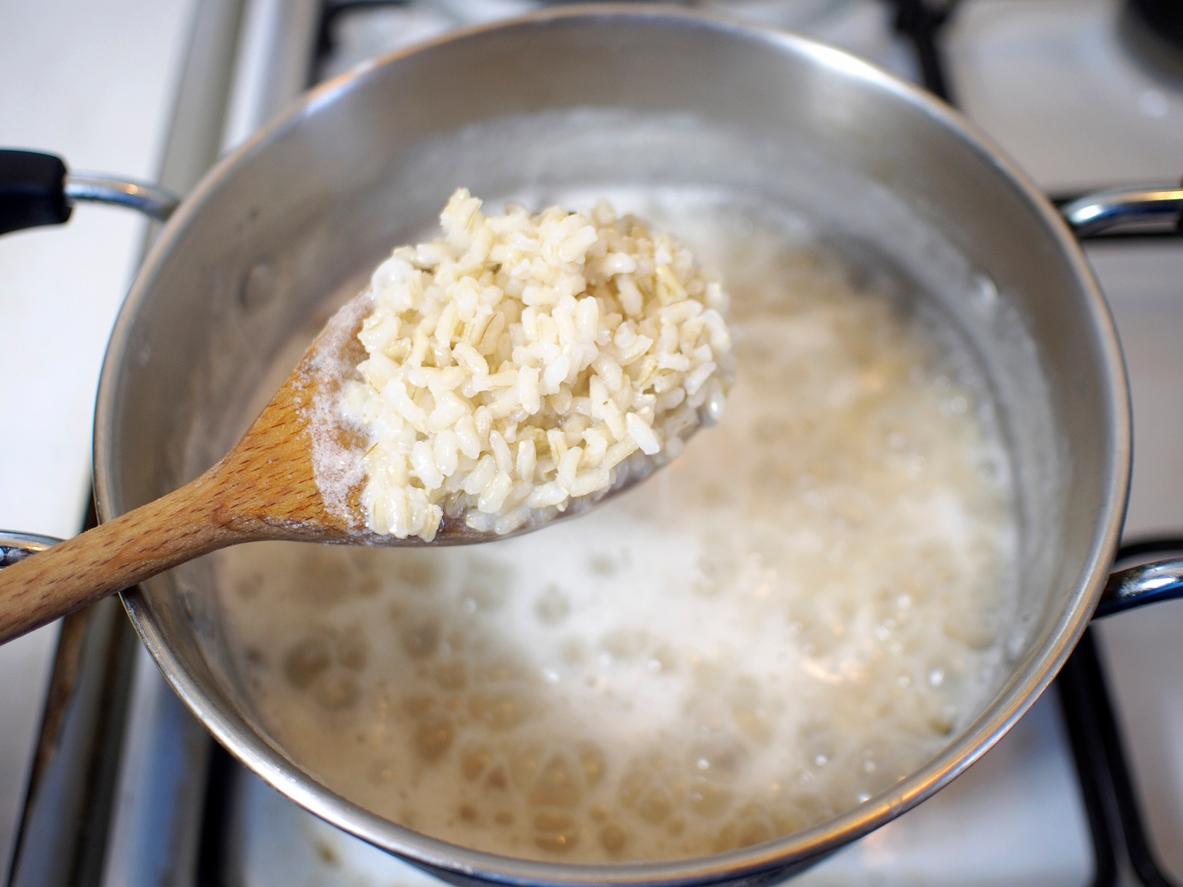 Close up of a wooden spoonful of rice with the rest of the boiling pot in the background.