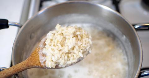 Close up of a wooden spoonful of rice with the rest of the boiling pot in the background.