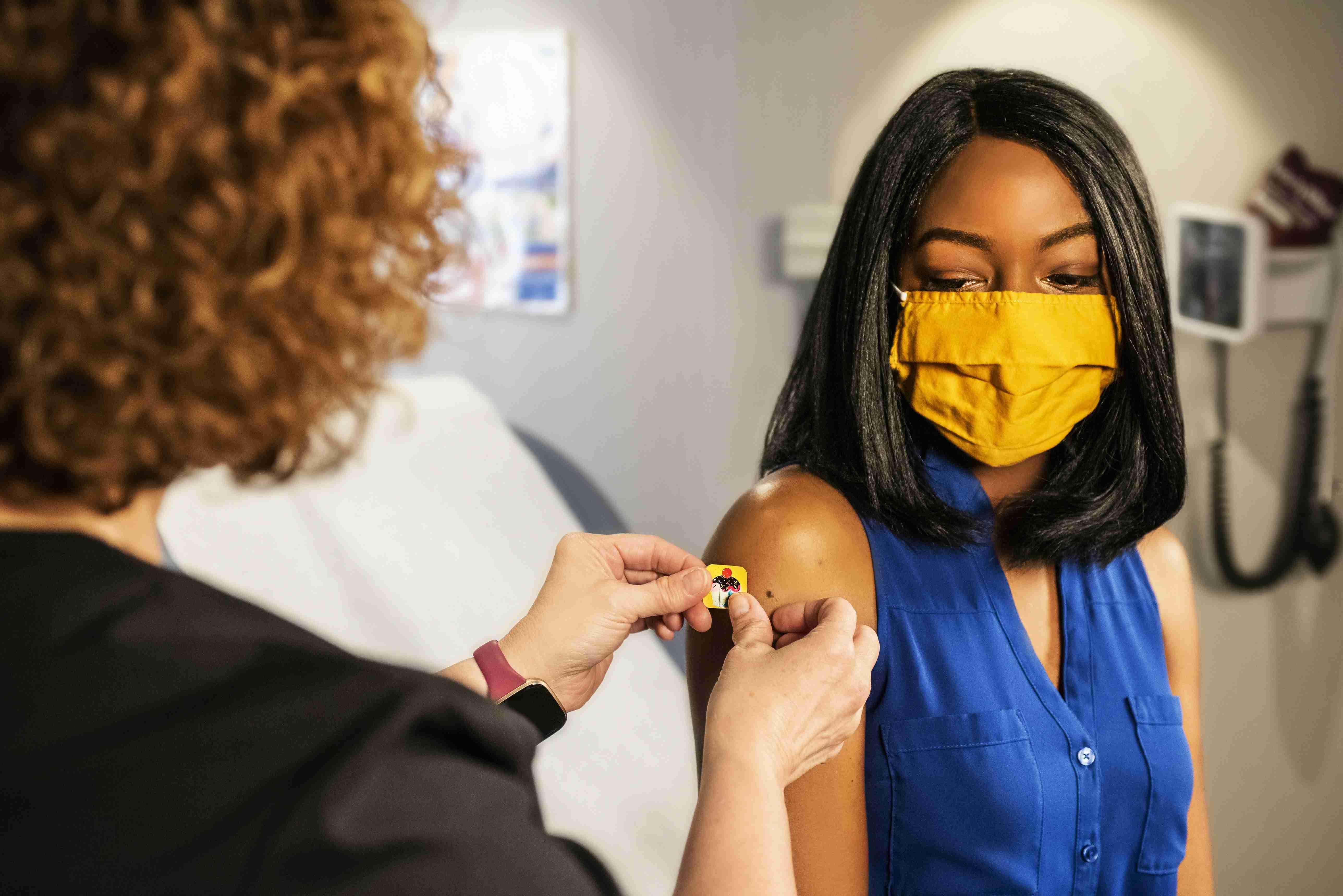 A woman with a cloth face mask receives a bandage after getting the COVID-19 vaccine.
