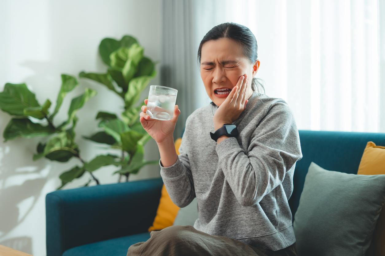 A woman winces as she holds her cheek after drinking water.