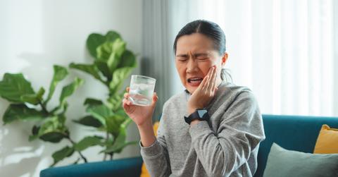 A woman winces as she holds her cheek after drinking water.