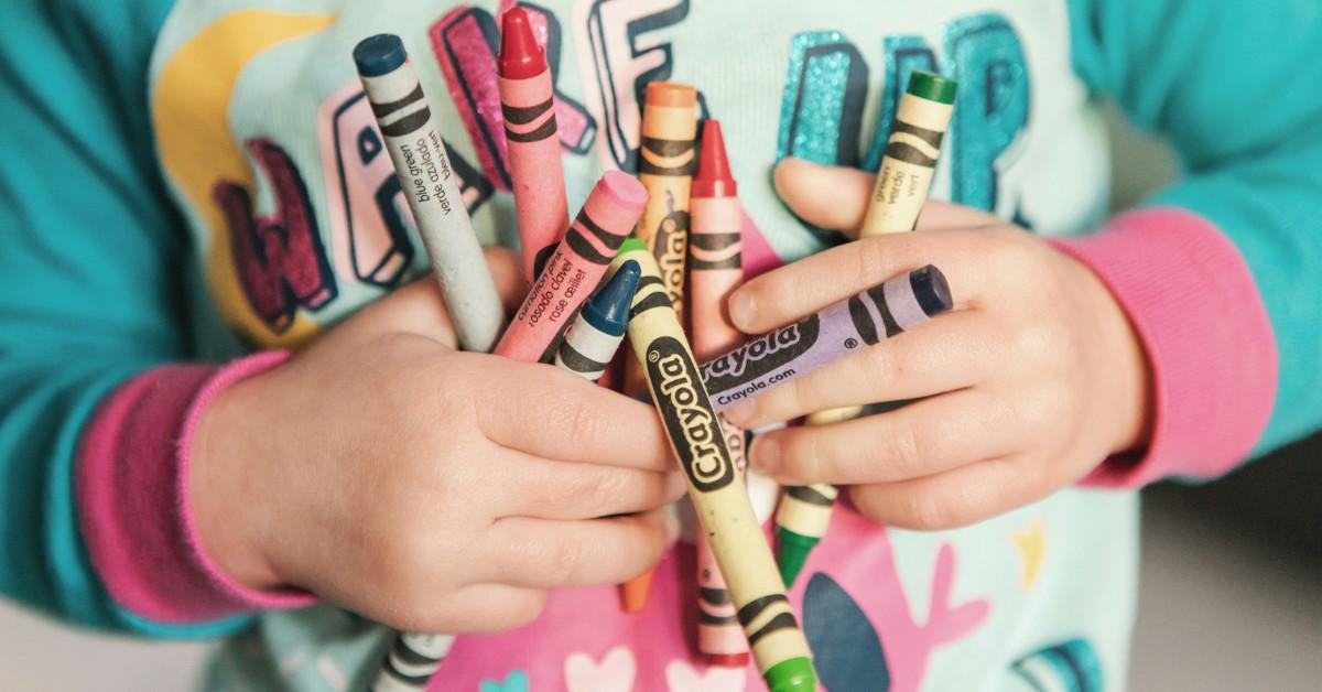 A little girl holds a bunch of Crayola crayons against her chest while she wears pjs