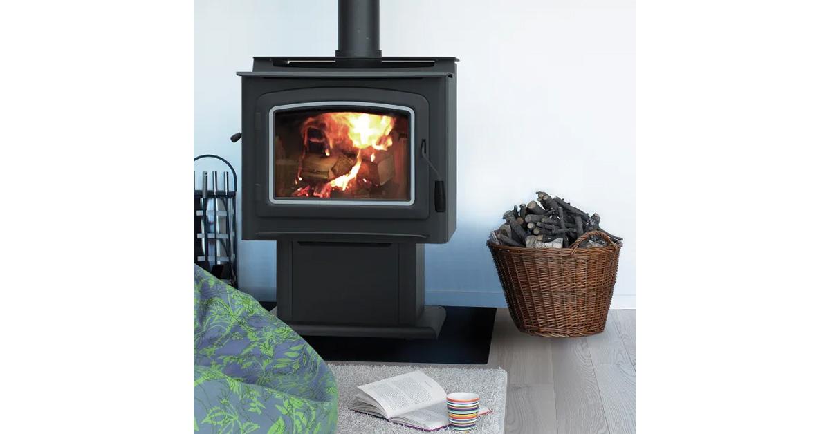 wood stove with fire inside and a basket of firewood with a book, mug, and blanket.