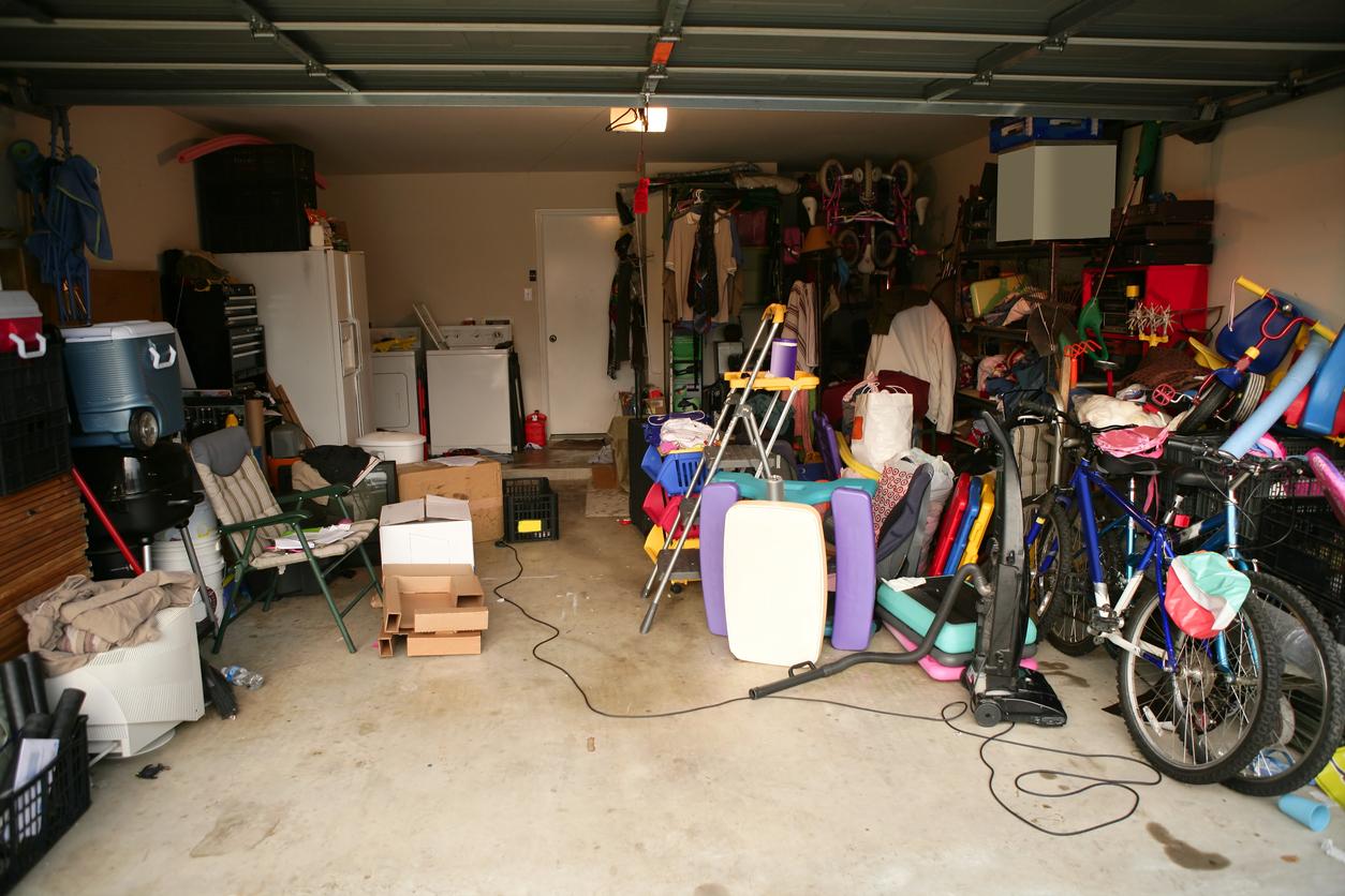 Coolers, bicycles, cardboard boxes, chairs, ladders inside a garage.