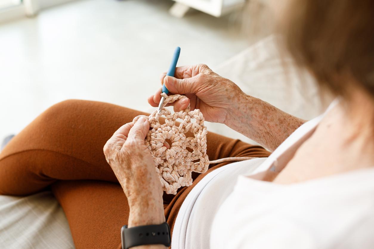 Person crocheting a light pink flower with a blue crochet hook.