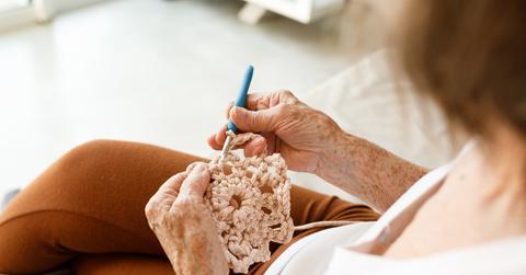 Person crocheting a light pink flower with a blue crochet hook.