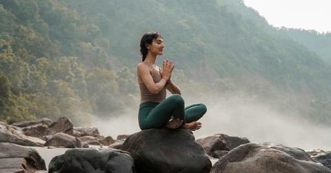 A woman sits atop a rock meditating