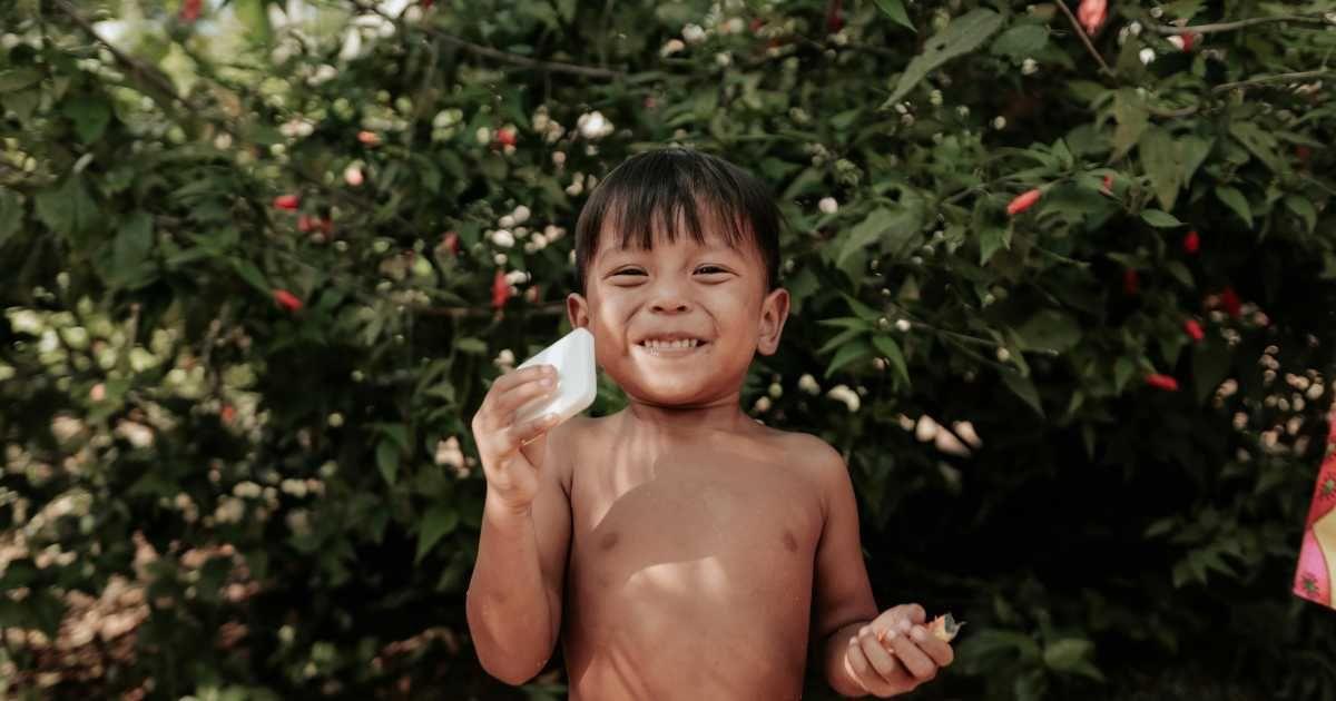 A little boy is smiling while holding a bar of soap, standing in a garden. (Representative Cover Image Source: Pexels | Luis Quintero)
