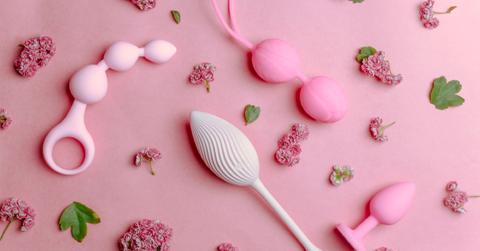 Photo of various pink sex toys surrounded by flowers and leaves over a pink background