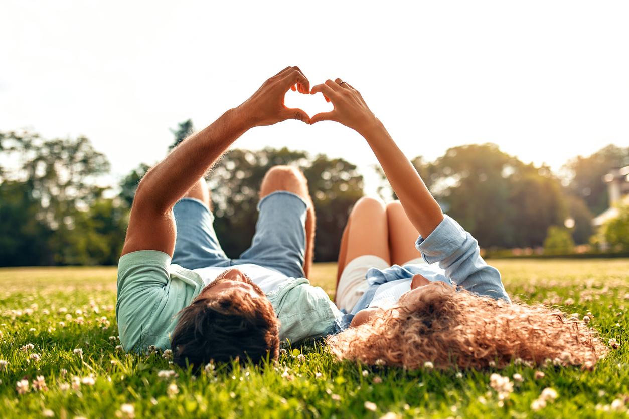 A man and woman lay on a field of grass together with their hands forming the shape of a heart.