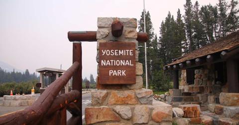 Yosemite National Park sign dangling on a brick structure in front of a hut (Representative Cover Image Source: Getty Images | WillEye)