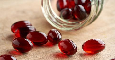 Red krill oil pills spilling from a glass container.