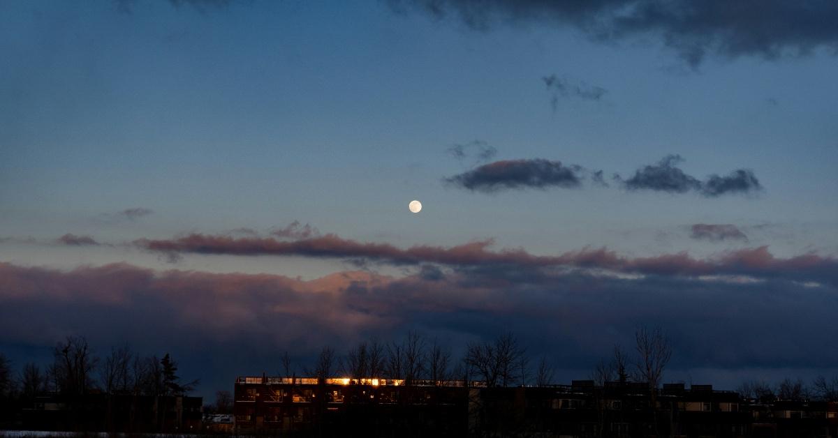 Silhouette of trees and buildings during sunset with full moon in the background. 