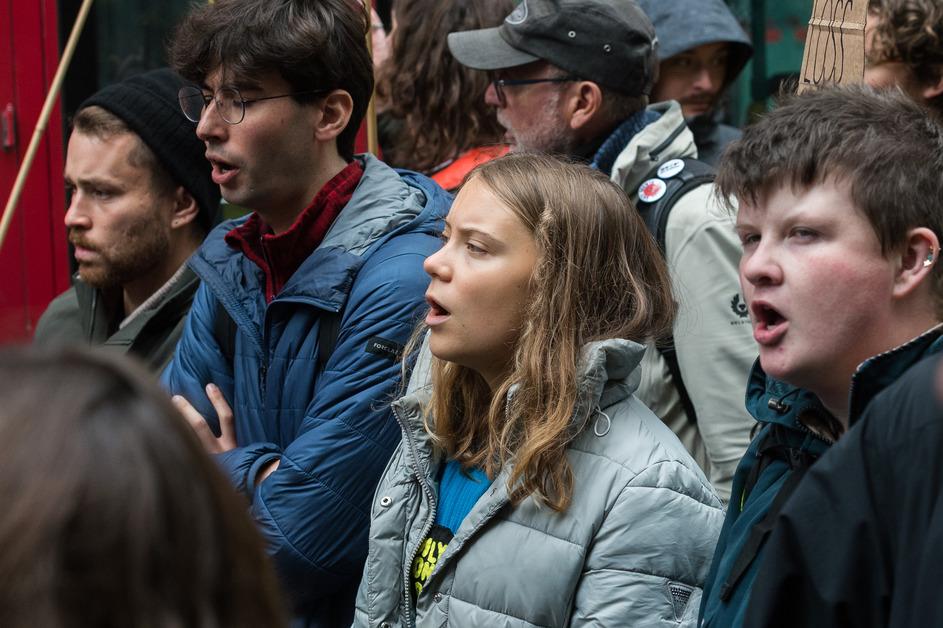 Greta Thunberg stands in between a crowd of other activists, all with their mouths open. 