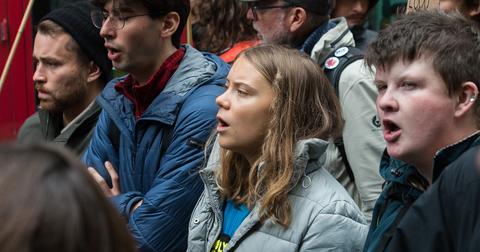 Greta Thunberg stands in between a crowd of other activists, all with their mouths open.
