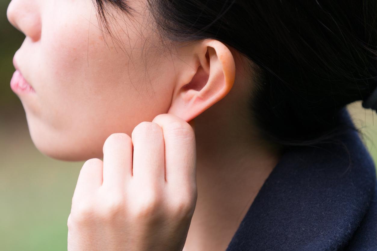 A woman is pictured tugging at her earlobe with her left hand.