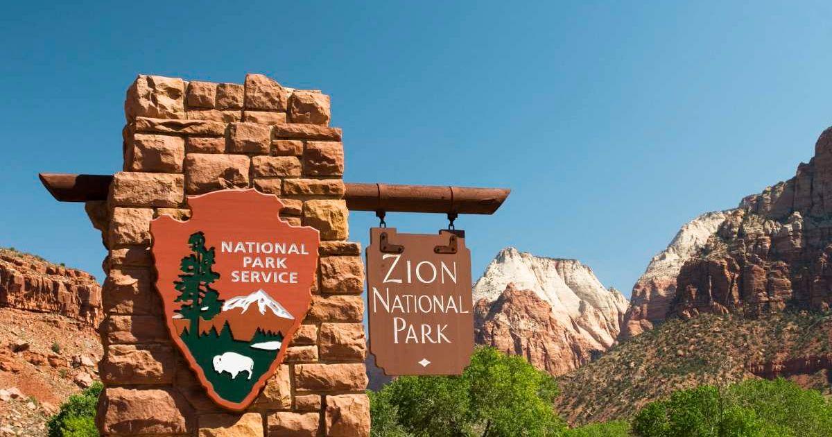 Sign reading Zion National Park hanging from a rocky wall (Representative Cover Image Source: Getty Images | Sageelyse)