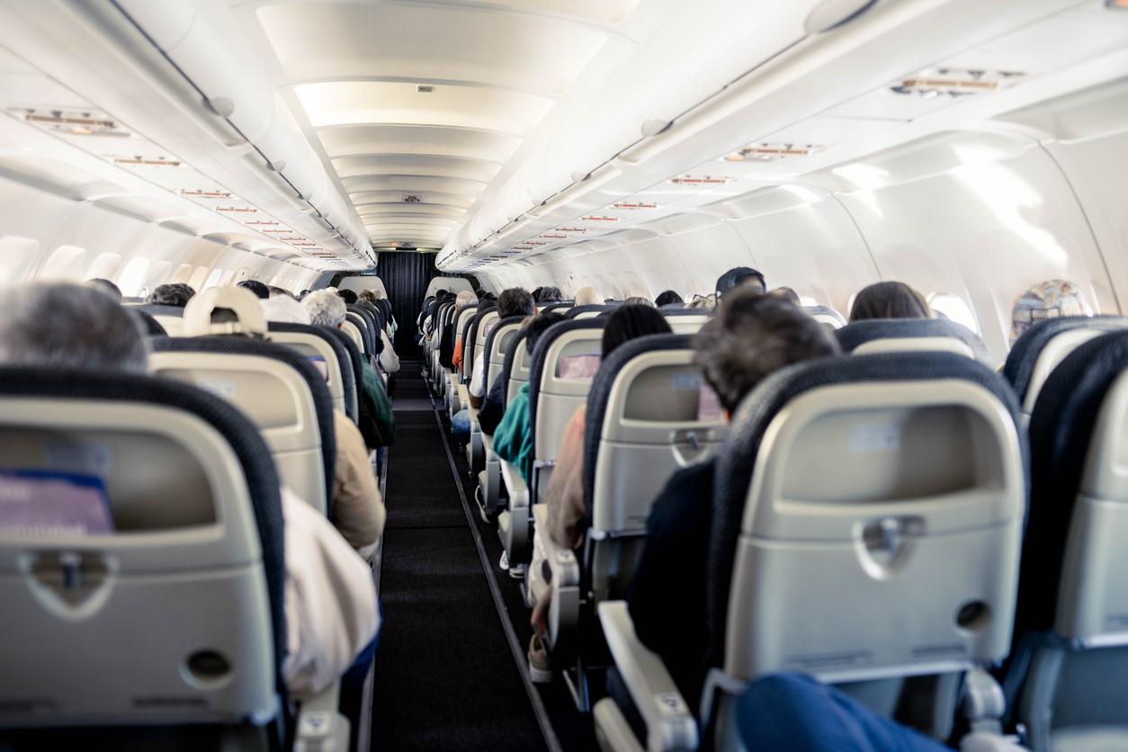 Rows of passengers are pictured from behind while sitting on an airplane.