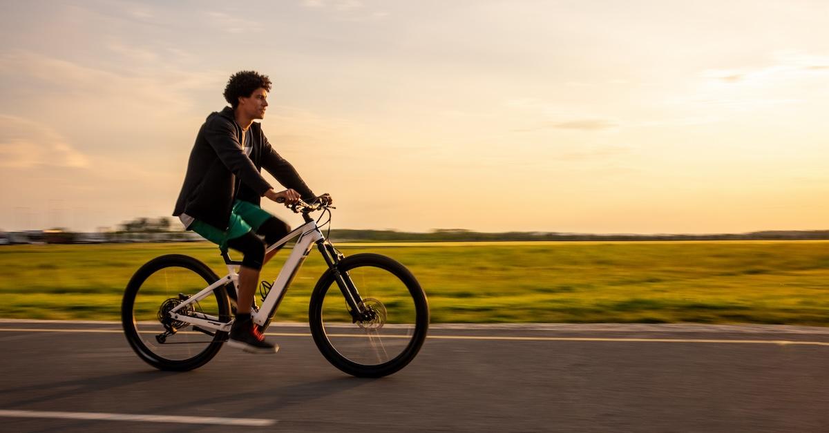 Young man rides e-bike along rural road with sunset in background